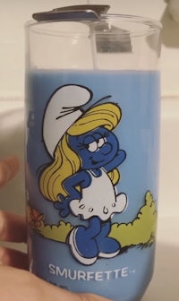 a person is holding a glass with a smurfite candle in it